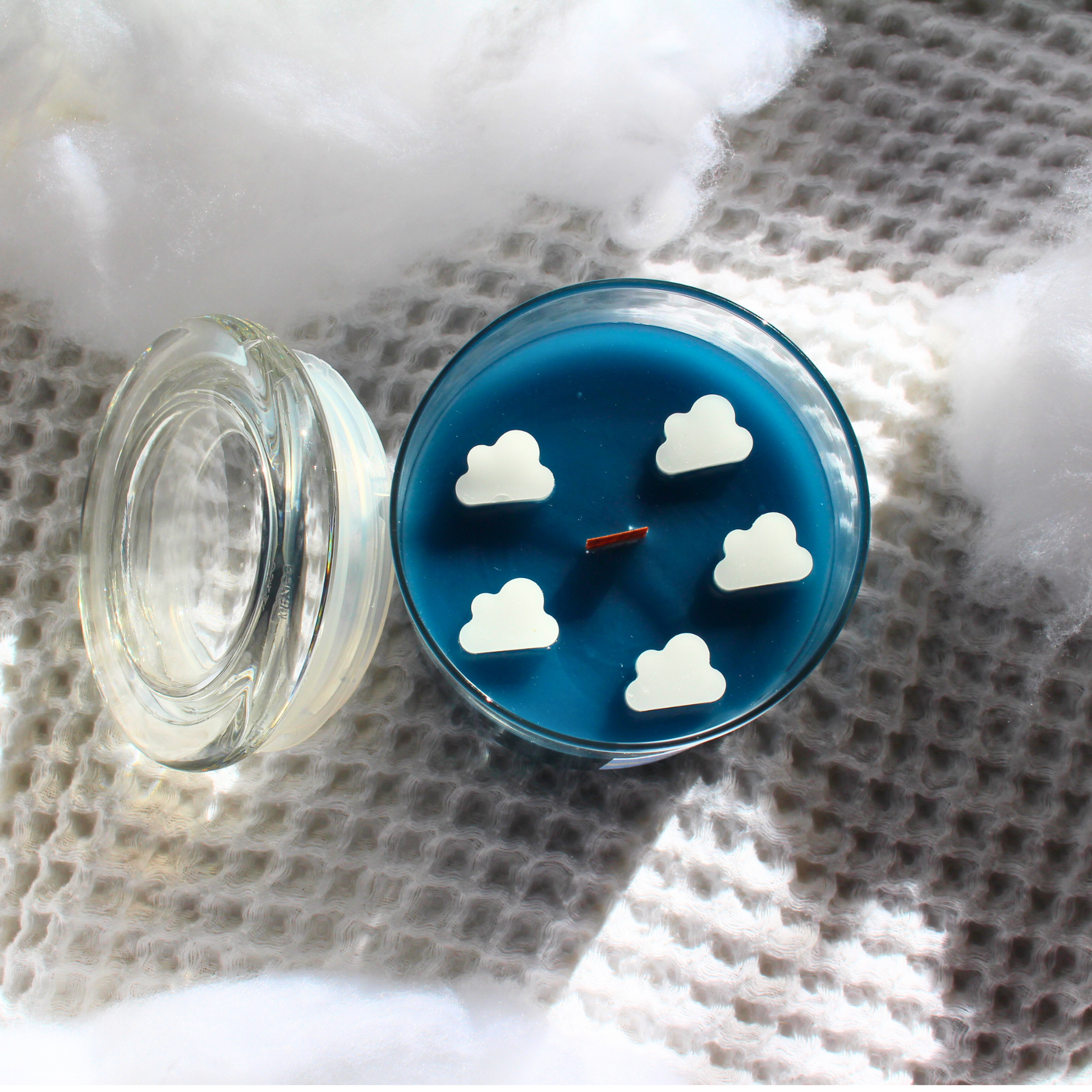this is a top view of our breezy bunny candle you can see white cloud embeds surrounding a wooden wick the wax is dark blue in a glass container vessel