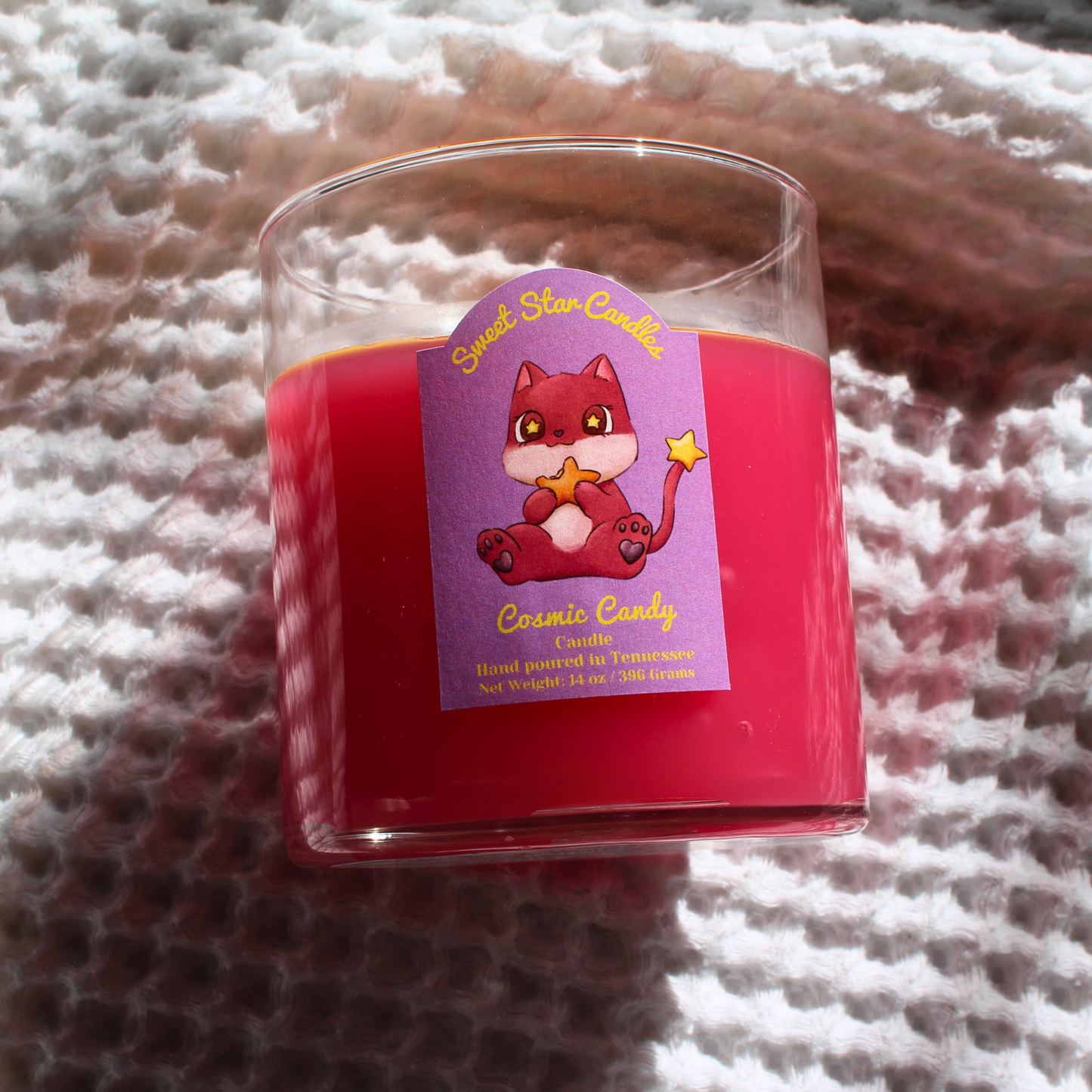 our cosmic candy pink candle the label is off the label is light purple the top reads in yellow letters sweet star candles under that is our custom character he is pink with cat ears and is eating a star he also has a star tail under that is reads cosmic candy the scent hand poured in tennessee and net weight 14 ounces