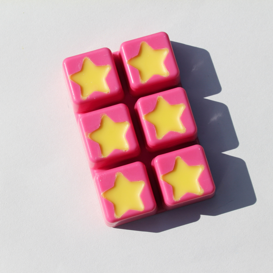 our cosmic candy wax melt out of the clamshell it features a pink soy wax background with yellow stars on top
