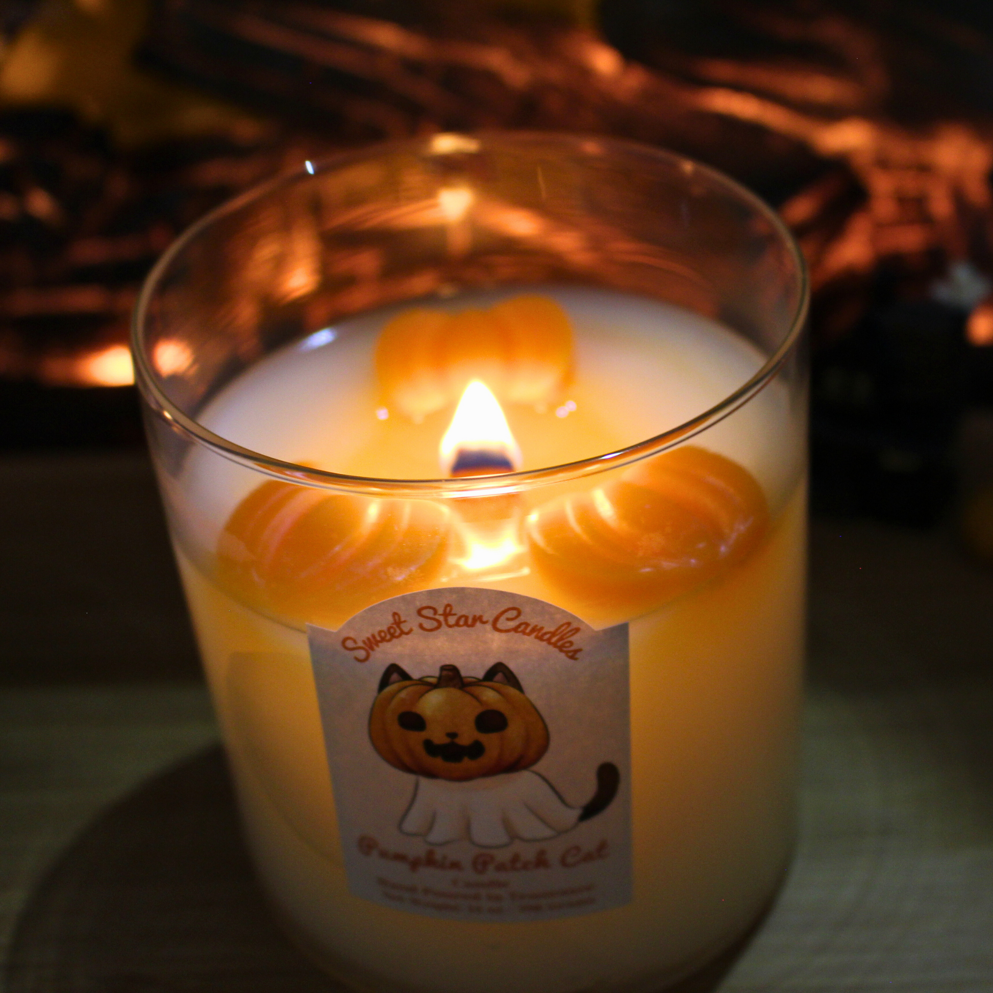 Candle with a pumpkin-themed label in front of a fireplace
