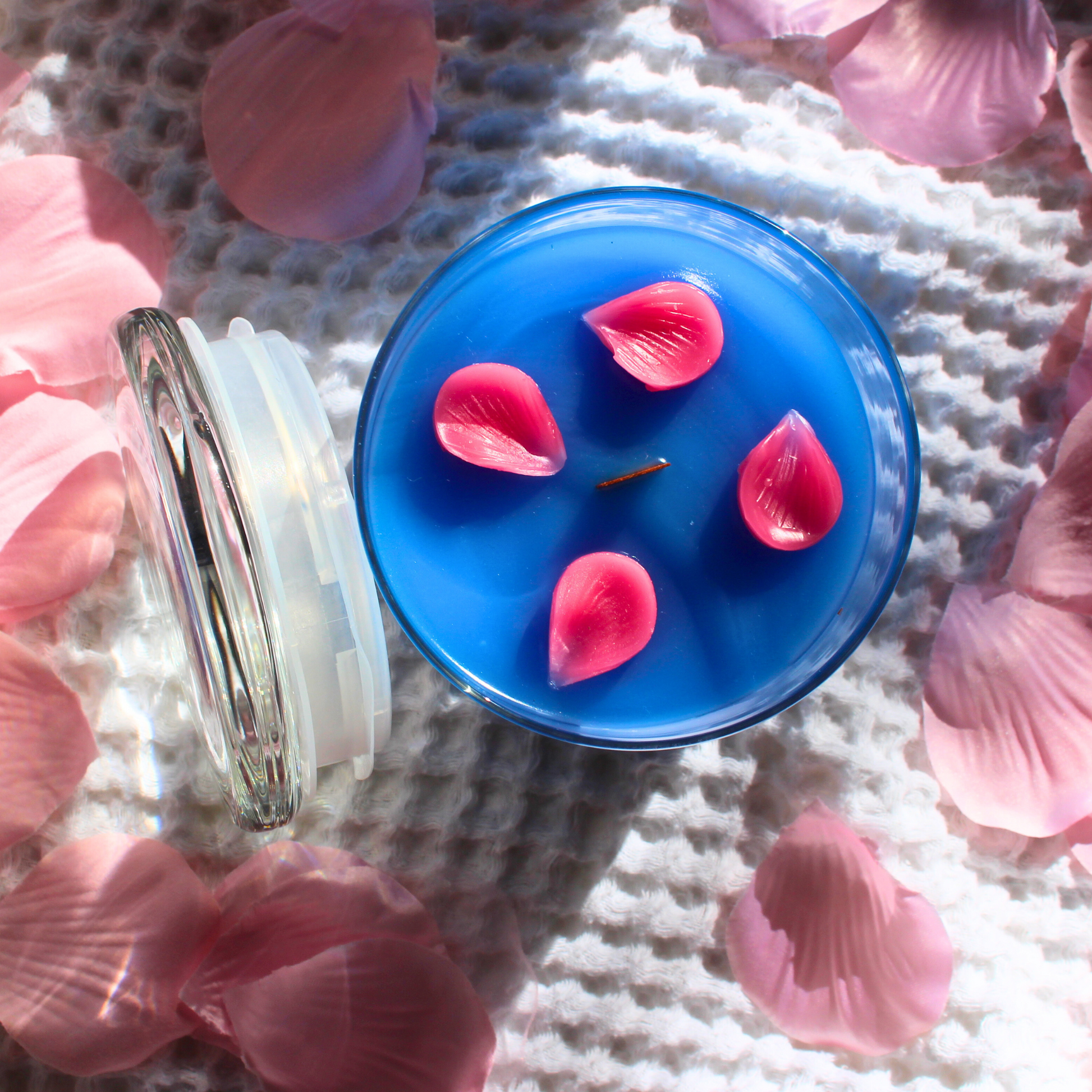 This shows a top view of the candle 4 cherry blossom petals can be seen scattered over the blue wax surrounding the wooden wick