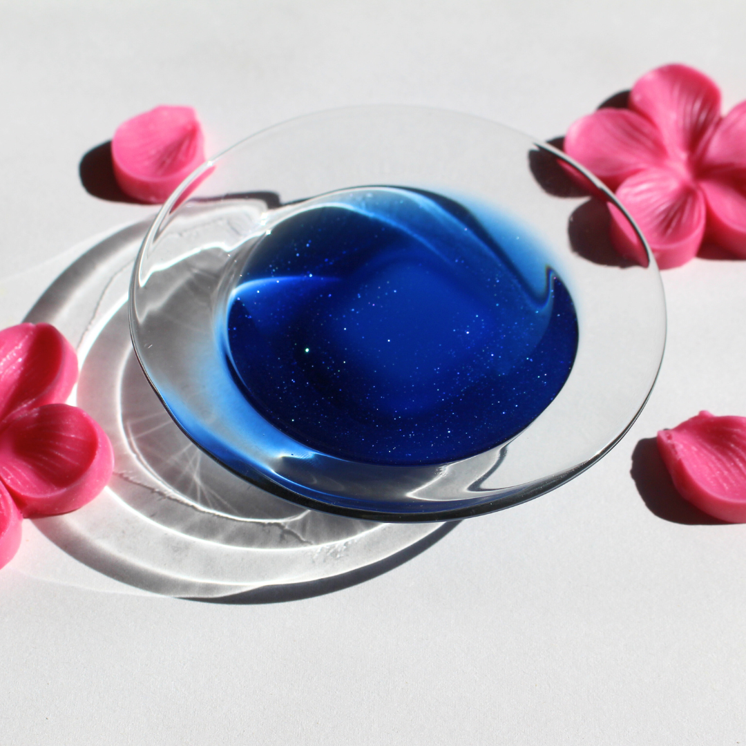 our sakura shiba wax melt fully melted in a wax warmer the wax is light blue and sparkles can be seen in the melted wax wax flowers are scattered in the background