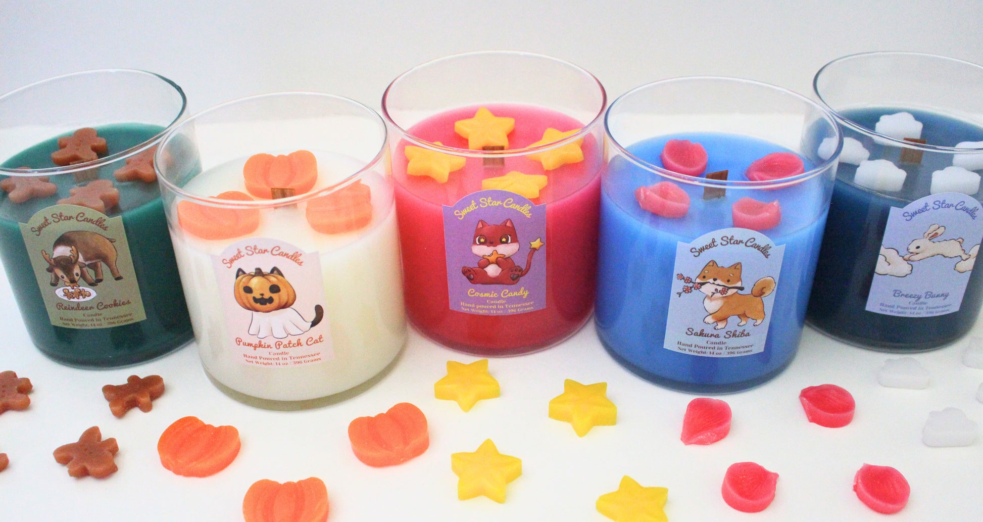 our candles are lined up from left to right our reindeer cookies candle pumpkin patch cat candle cosmic candy candle sakura shiba candle breezy bunny candle each candle has embeds in front of it from the correlating scent for example the cosmic candy candle has star embeds in front of it