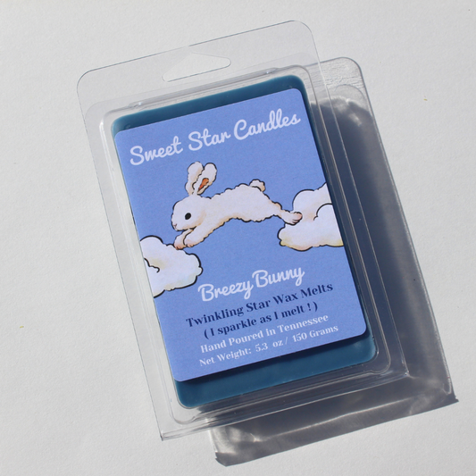 our breezy bunny wax melt from the front you can see the label which is blue and light blue at the top it says sweet star candles in white font underneath a white bunny can be seen jumping from one white candle to another his fur looks like it is made of clouds underneath the bunny is the title breezy bunny under the title is the words twinkling star wax melts i sparkle as i melt underneath that it lets you know the wax melt is hand poured in east tennessee and is a 5.3 ounce wax melt or 150 grams 