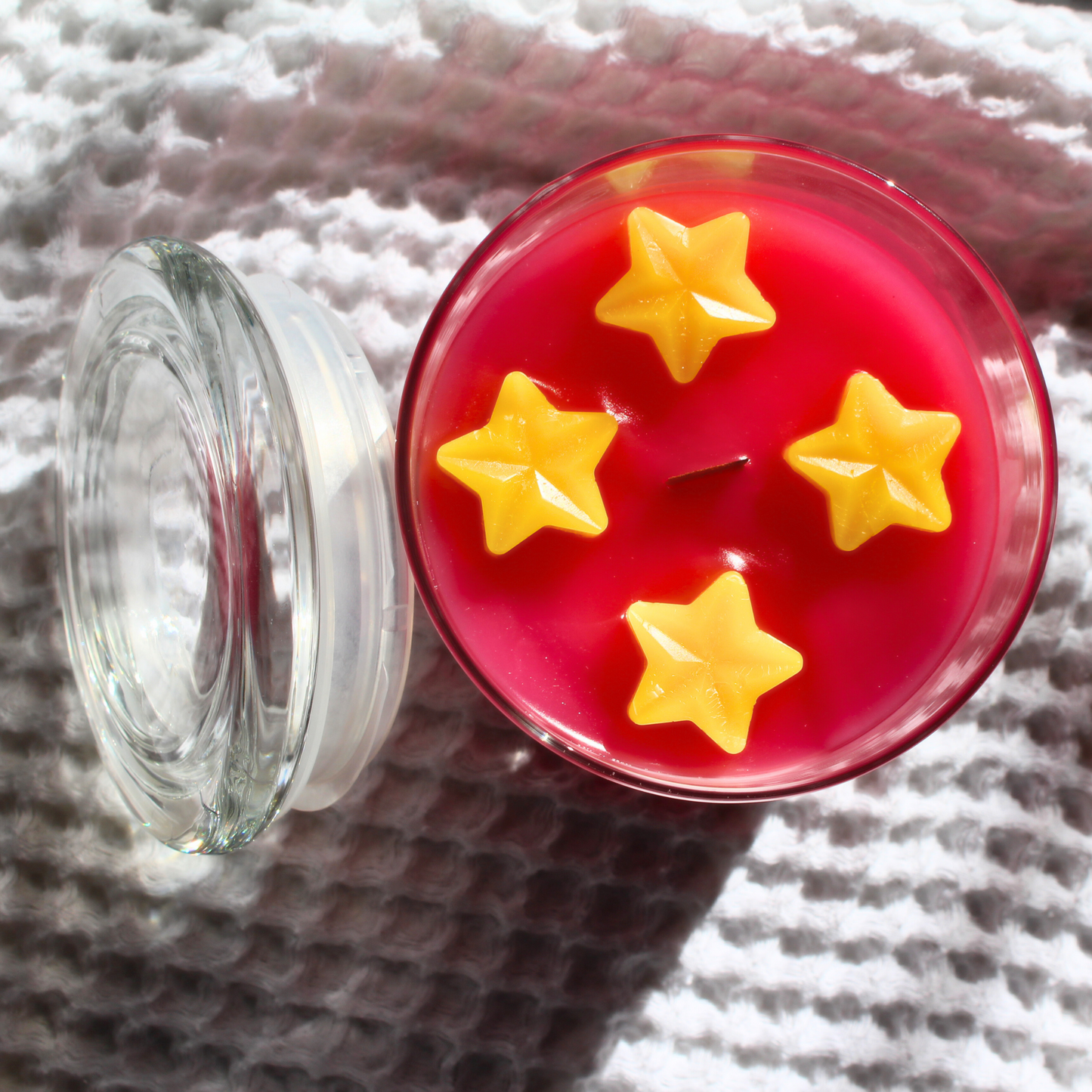 This shows a top view of the candle 4 yellow stars go around the wooden wick in the center of the candle atop the magenta colored candle below