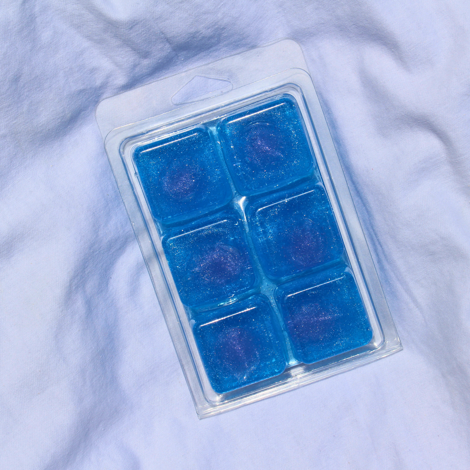 Pack of blue jelly wax melts on a light purple fabric background