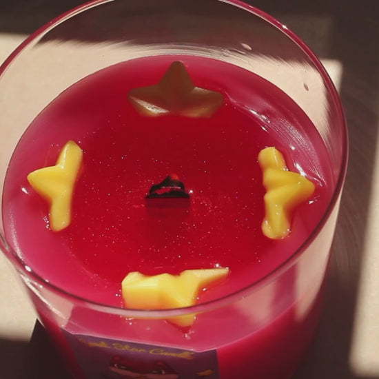 our cosmic candy candle sparkles as it melts yellow stars can be seen around a pool of melted sparkly wax as the wooden wick flickers 