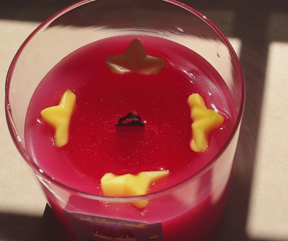 our cosmic candy candle sparkles as it melts yellow stars can be seen around a pool of melted sparkly wax as the wooden wick flickers 