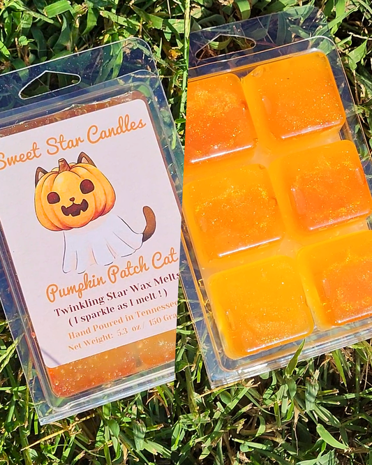 Two clear plastic wax melt clamshells on grass. One package shows the front label reading 'Sweet Star Candles Pumpkin Patch Cat' with a pumpkin illustration, and the other shows six orange wax cubes inside a clamshell.