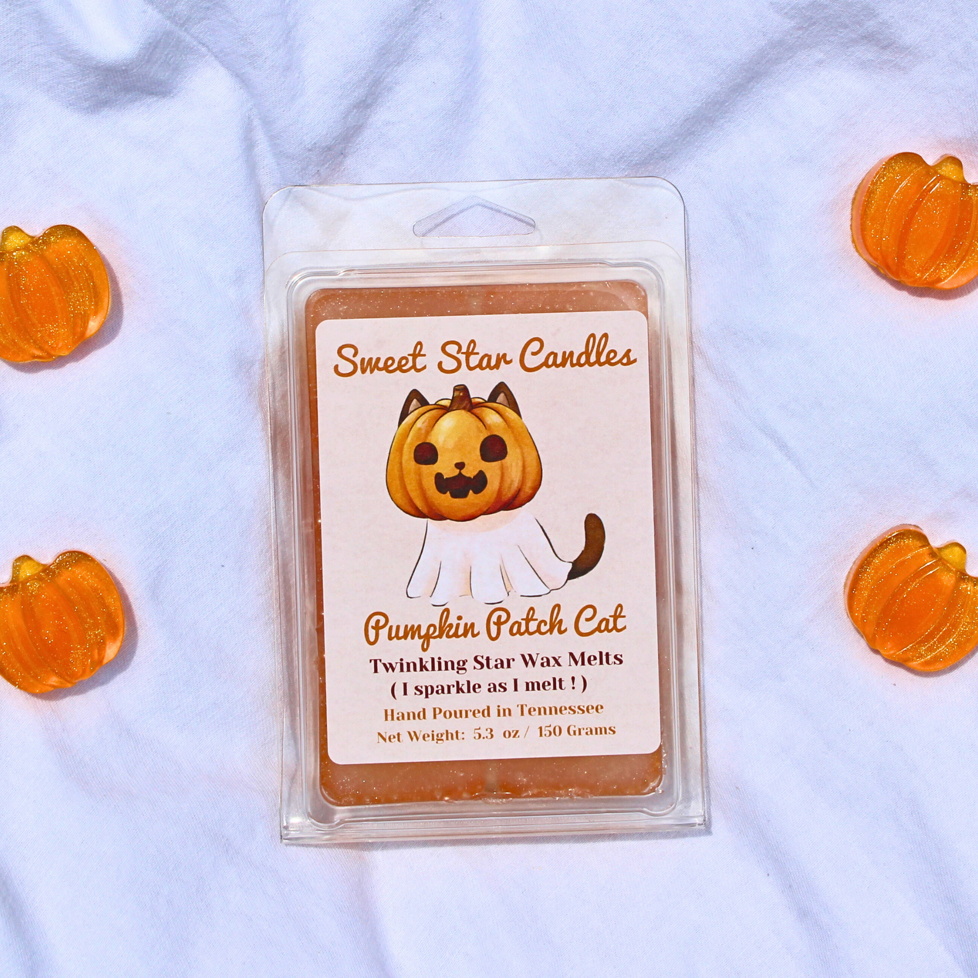 A clear package of Twinkling Star wax melt with a label featuring a cartoon cat in a pumpkin patch. The package is surrounded by small orange pumpkin decorations.