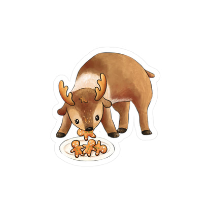 A die-cut sticker featuring a cute cartoon reindeer eating gingerbread cookies from a white plate, shown on a plain white background.
