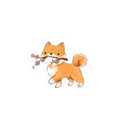 A die-cut sticker featuring a cute watercolor illustration of a Shiba Inu dog holding a branch with pink blossoms in its mouth, shown on a plain white background.