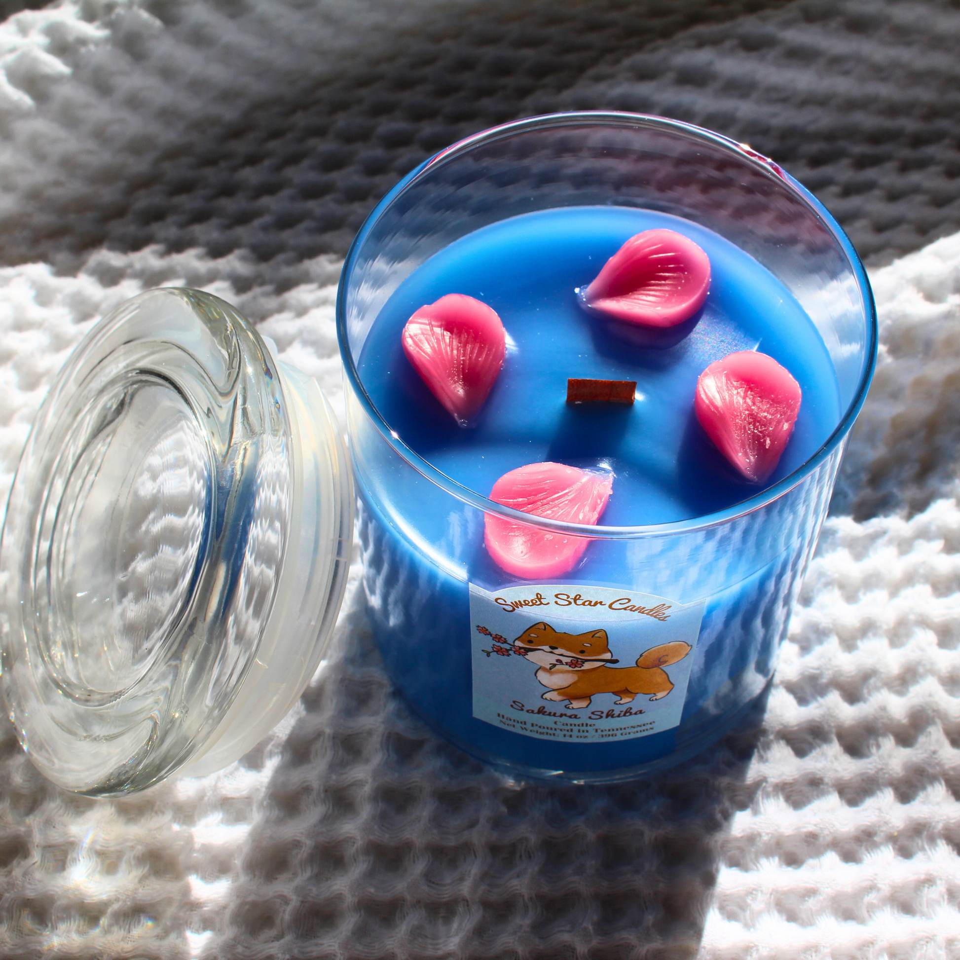 Blue candle with pink petals in a glass jar on a textured surface with a shiba inu label