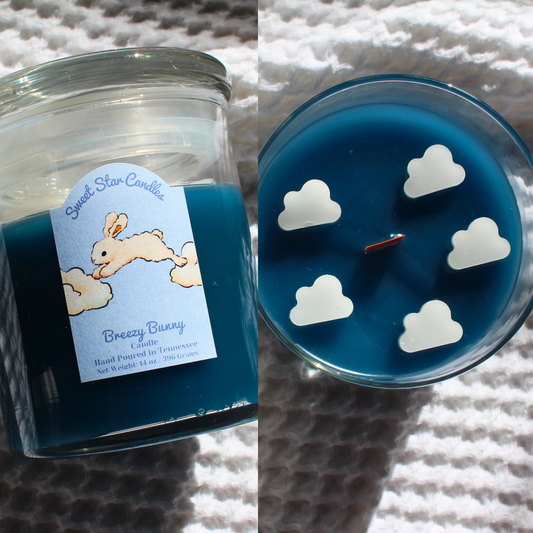 our breezy bunny sparkle as it melts candle sits on a white background with clouds the label reads sweet star candles with a bunny underneath jumping from cloud to cloud under that it says breezy bunny candle hand poured in tennessee net weight 14 ounces the label is light blue with a white bunny the wax is dark blue in a glass vessel