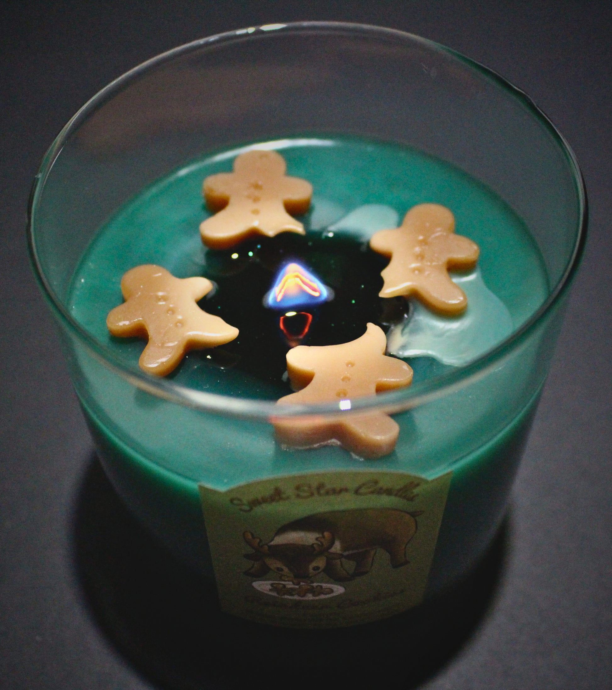 The dark green wax is melting around the wooden wick little sparkles can be seen in the wax as it melts.