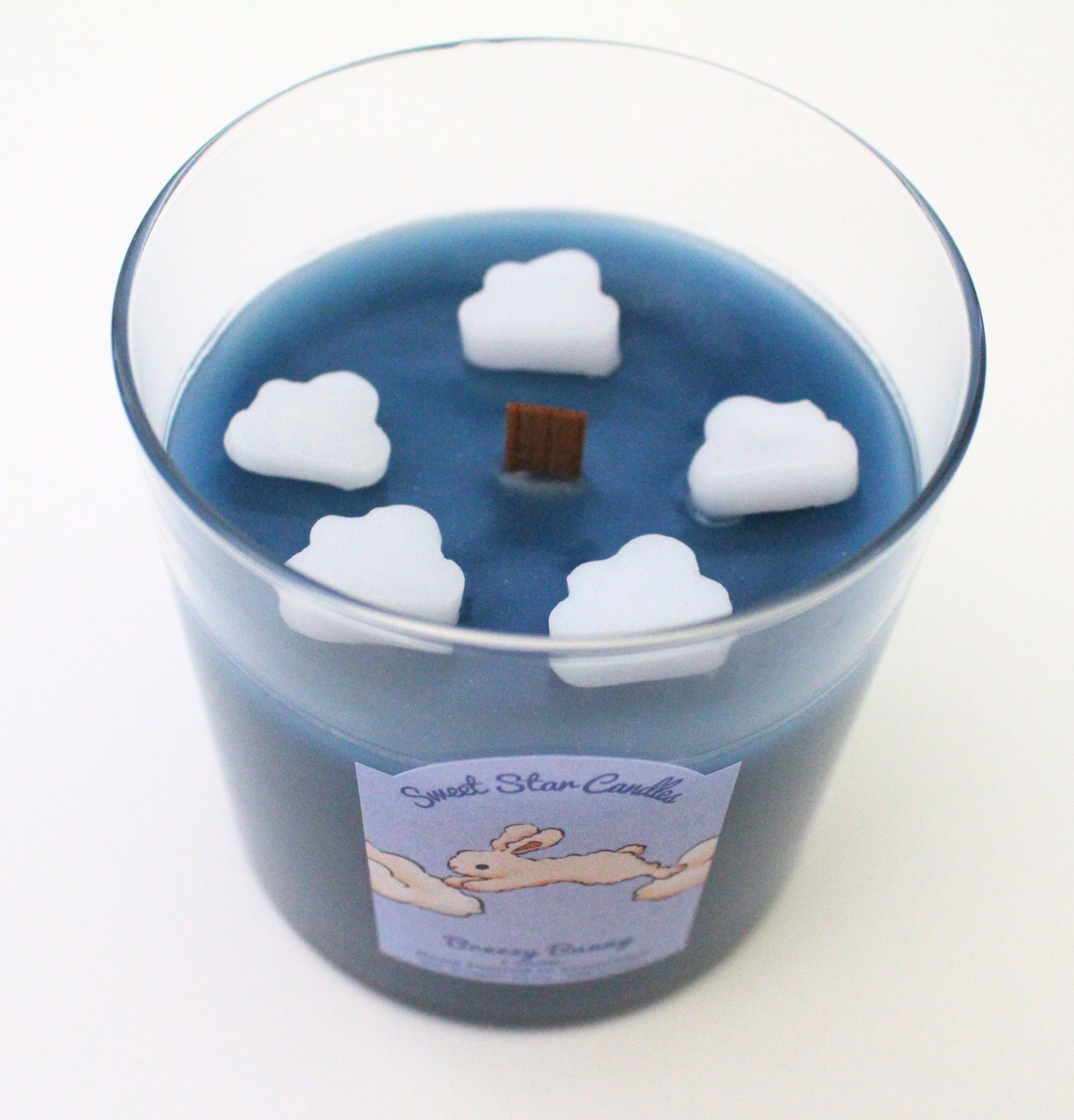 White clouds sitting on top of the dark blue wax 5 clouds go around the wooden wick at the top of the candle