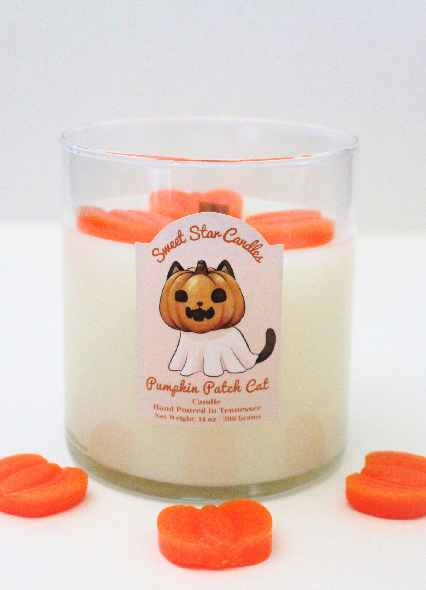 our pumpkin patch cat candle sits surrounded by orange wax pumpkins the pumpkins and wooden wick can be seen through the glass jar