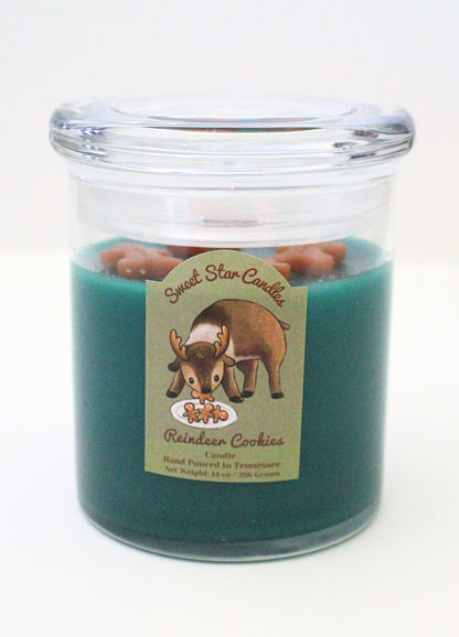 This shows a dark green candle with light brown gingerbread men sitting on top the label features a reindeer stealing gingerbread men from santas plate the label also states sweet star candles reindeer cookies candle hand poured in tennessee with a net weight of 14 ounces.