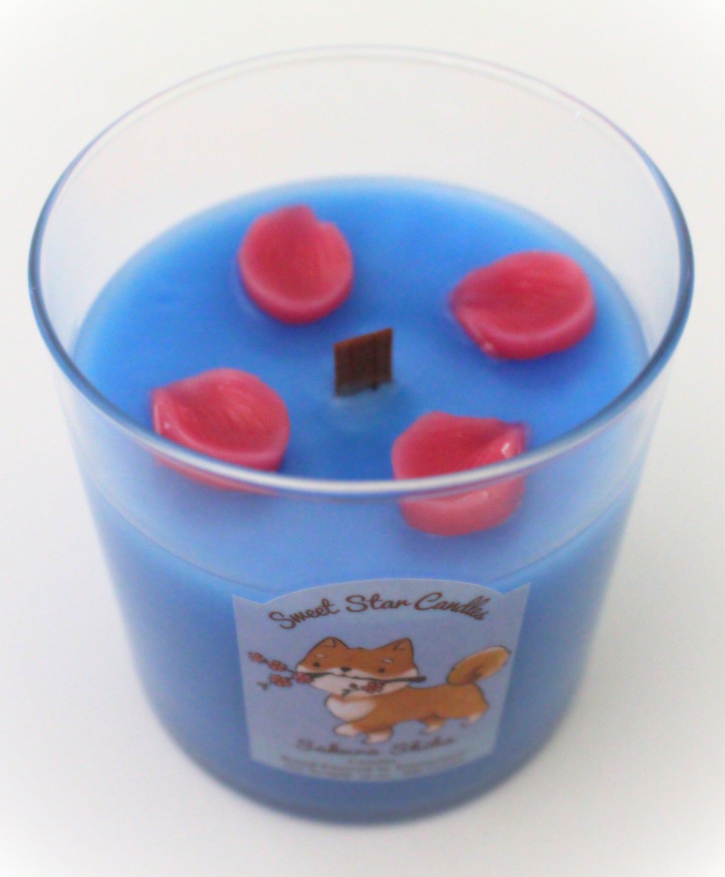 This shows a top view of the candle 4 cherry blossom petals can be seen scattered over the blue wax surrounding the wooden wick